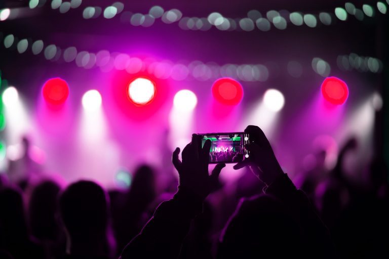 Person recording a concert in Seattle with a smartphone, capturing the stage lights and crowd silhouette.