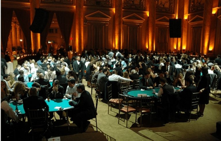 Elegant event in a grand hall with guests seated around tables, chatting and dining under warm ambient lighting.