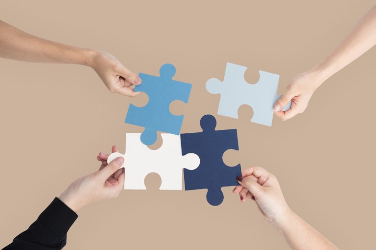 Four hands connecting large puzzle pieces against a neutral beige background in a corporate Seattle office.