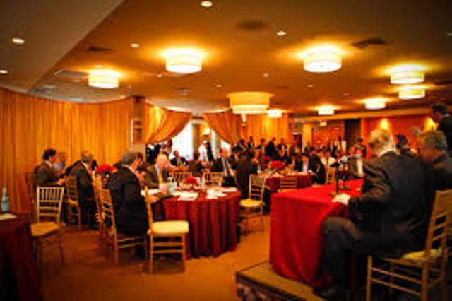 Business professionals gathered in a banquet hall with red tablecloths during a formal event.