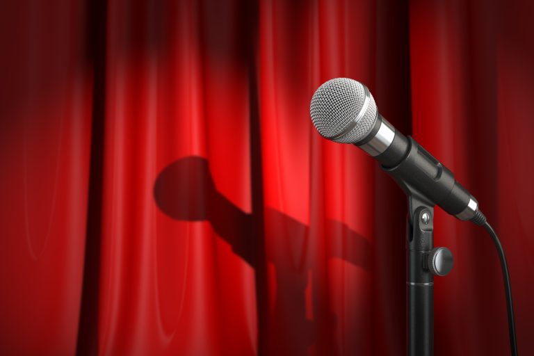 Microphone on a stand with shadow cast on a closed red curtain background, suggesting an entertainer's stage setting in Seattle.
