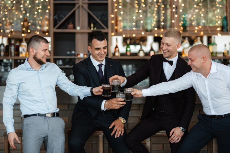 Four men in formal attire toasting with dark drinks at a bar in Seattle, smiling and enjoying the moment together.